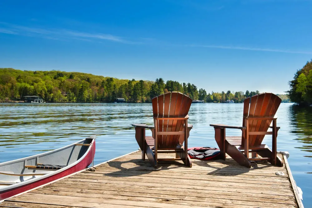 Two Adirondack chairs sitting on a dock overlooking a lake